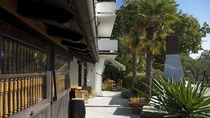 Un edificio con un espacio de estar al aire libre techado, mobiliario de madera y una palmera.