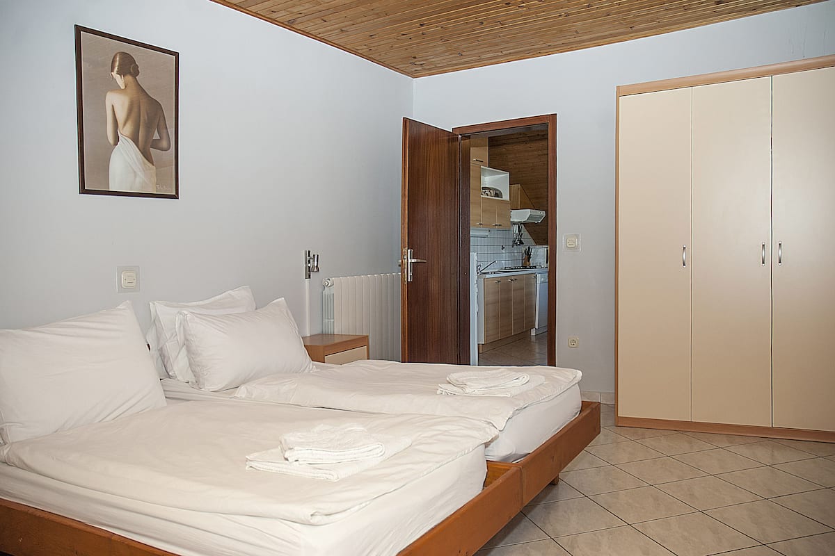 Un dormitorio con dos camas, un armario de madera y una cocina visible a través de una puerta abierta.