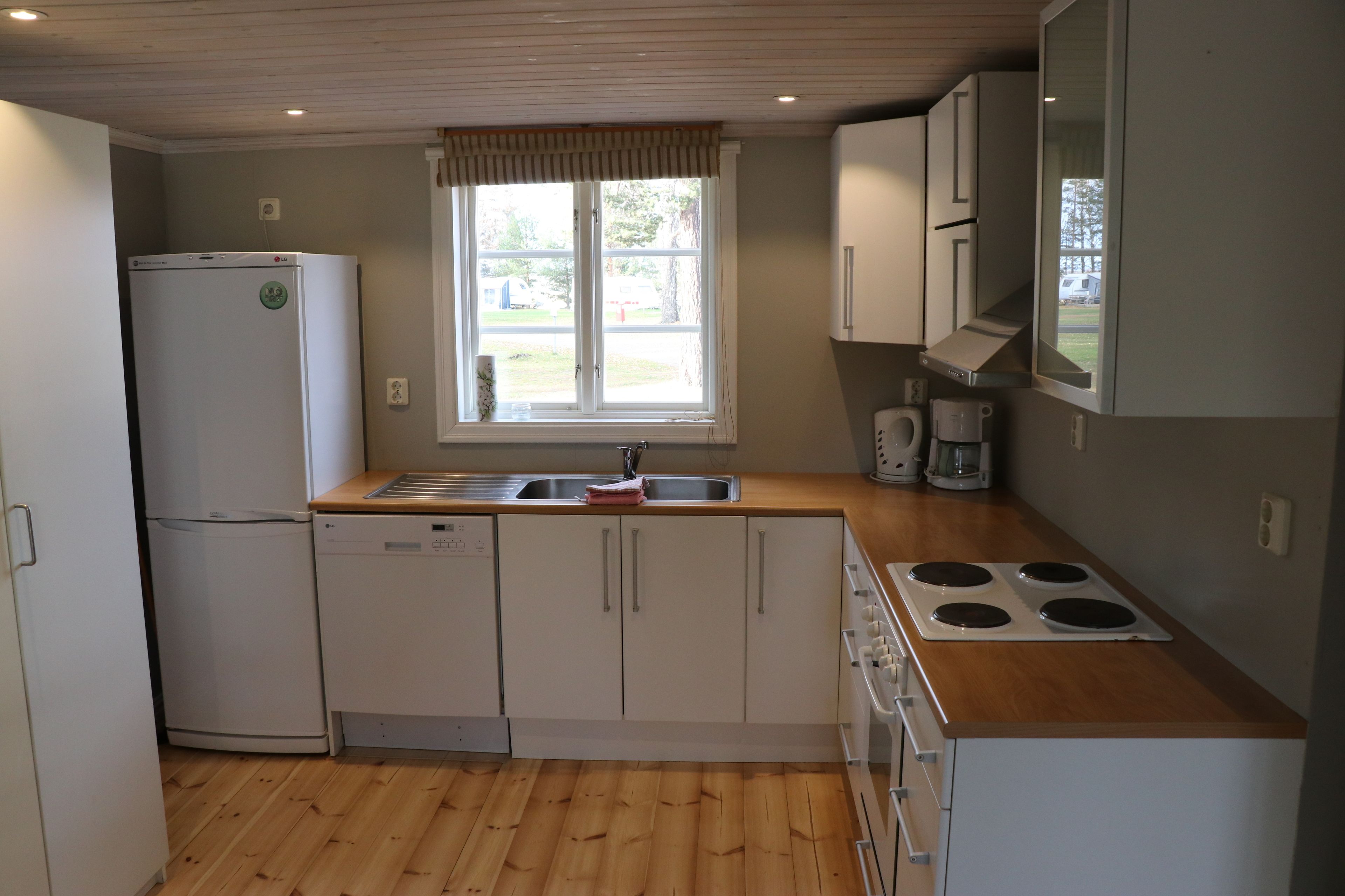 A compact kitchen with a refrigerator, dishwasher, stove, and a window providing natural light.