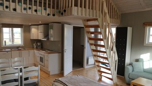 A compact, well-lit room with a kitchenette, a dining area, and a staircase leading to an upper level. - Ljusdals Camping (Ljusdal)