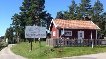 A red building with a tiled roof, a wooden fence, and a sign for Ljusdals Camping.
