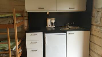 A compact kitchen with a coffee maker, sink, and white cabinets.