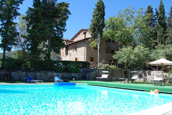 A swimming pool with lounge chairs and a stone building in the background.