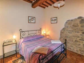 A bedroom with a bed, a nightstand, a lamp, and a stone wall.