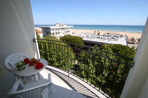 A balcony with a table and chairs, overlooking a beach and buildings. - Residence Angeli Rimini (Rimini)