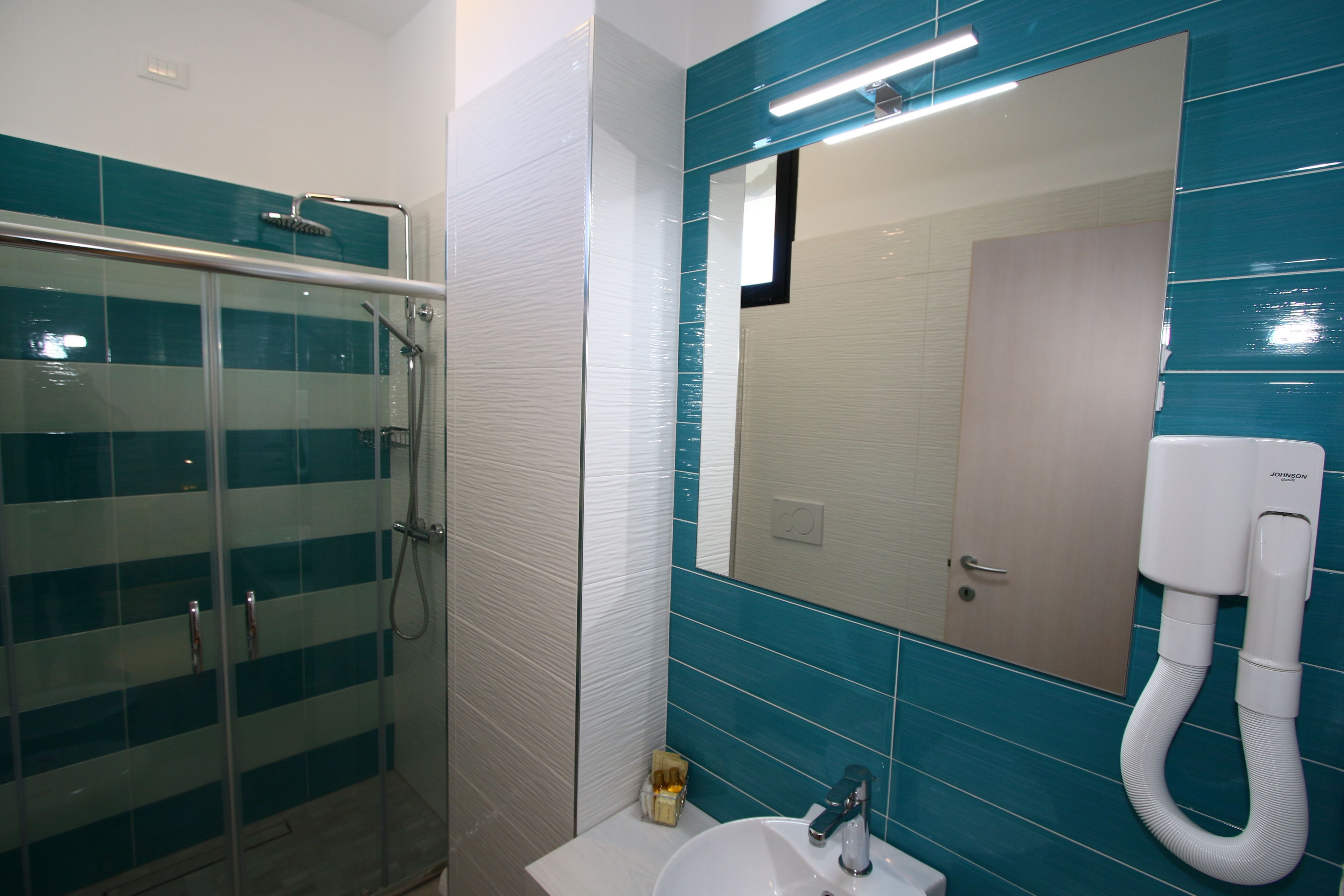 A bathroom with a glass shower enclosure, a sink, and a mirror with a built-in telephone.