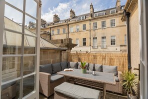 An outdoor patio with wicker furniture, a table, and a potted plant. - Crescent Mews (Bath)