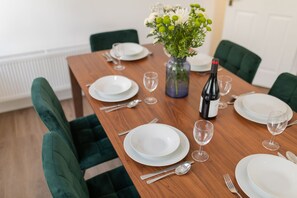 A dining table set with white plates, silverware, and a wine bottle, surrounded by green upholstered chairs. - Crescent Mews (Bath)