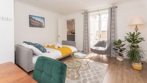 Una habitación de hotel moderna con una cama, un sillón verde, una mesita y una planta en maceta.