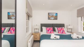 A double bed with teal bedding, two bedside tables with lamps, a mirror, and a framed picture of a bridge on the wall.
