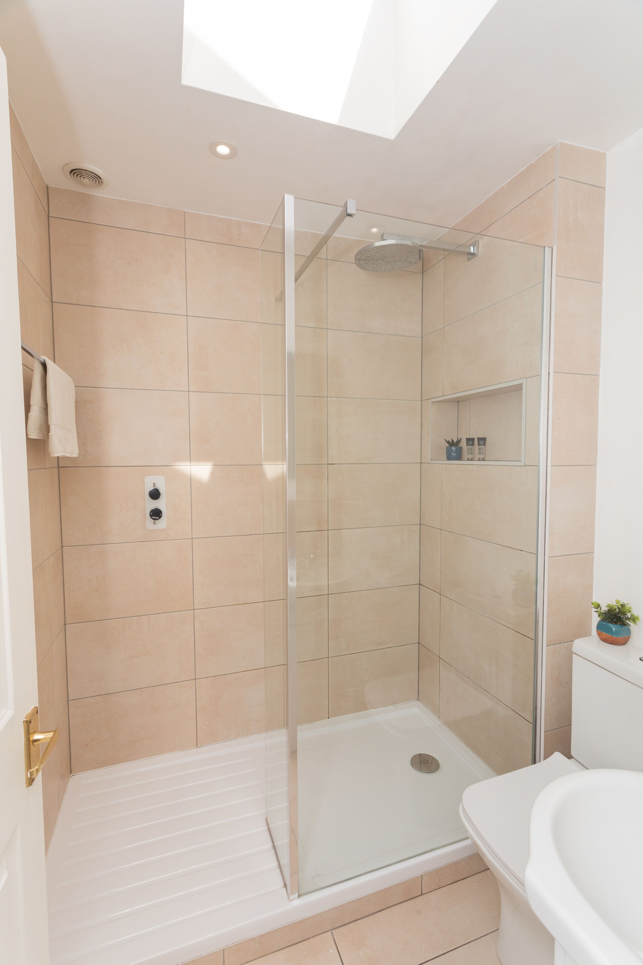 A modern bathroom with a glass-enclosed shower, a white bathtub, and beige tiles.