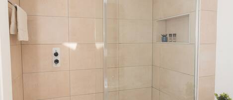 A modern bathroom with a glass-enclosed shower, a white bathtub, and beige tiles.