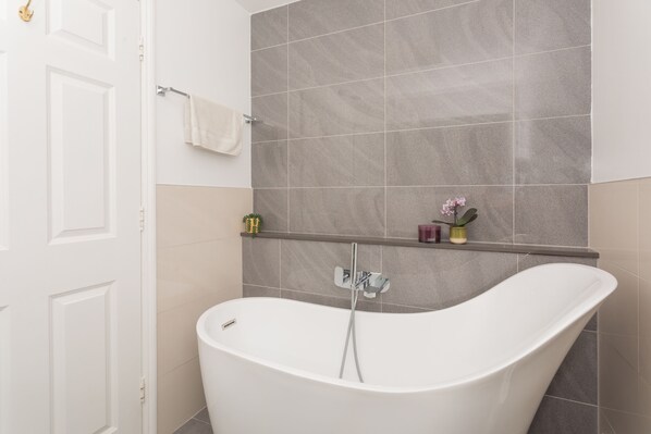 A modern bathroom with a freestanding bathtub, a towel rack, and a shelf with toiletries.