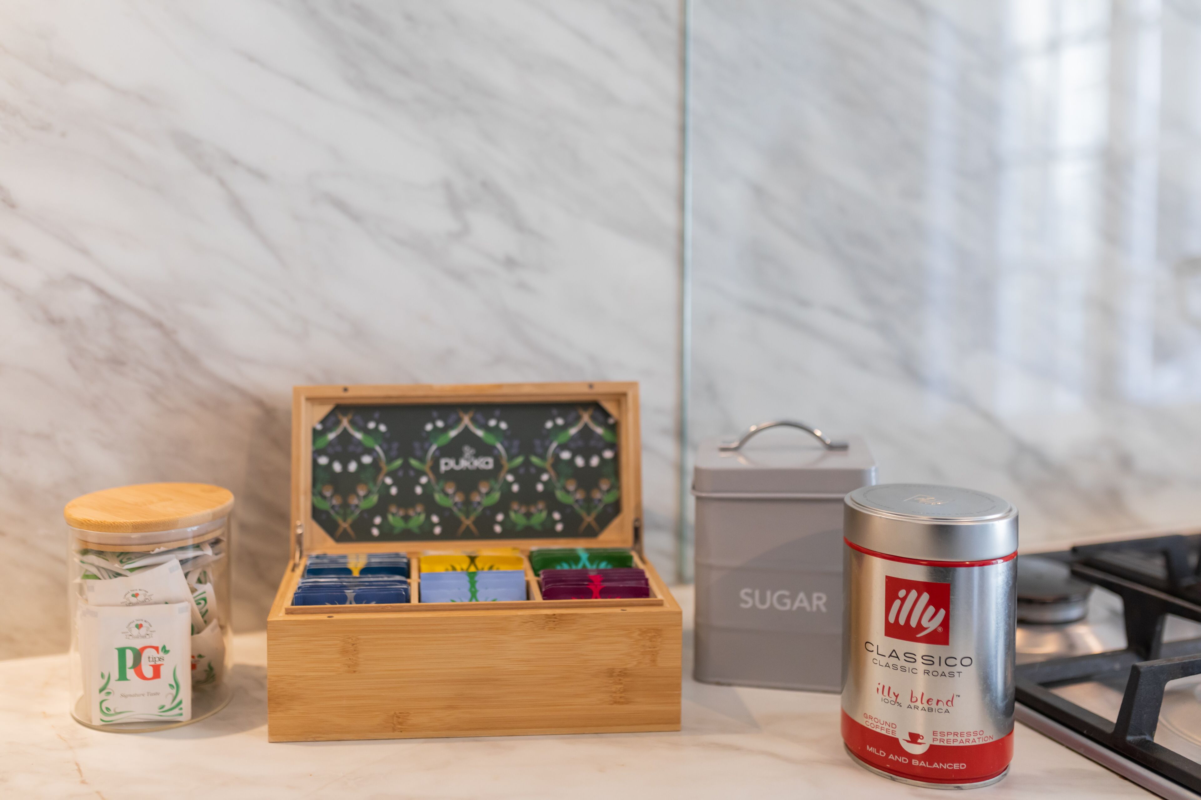 Een keukentrap met een koffiezetapparaat, een doos PG tips, een suikerdoos en een blik Illy koffie.