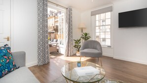 Una sala de estar moderna con un sillón gris, una mesa de centro de vidrio y un televisor de pantalla plana en la pared.