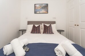 A neatly made bed with white linens and two patterned pillows, a blue blanket, and two white towels. - Crescent Mews (Bath)