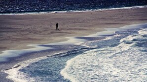 Una playa con una persona caminando sobre la arena.
