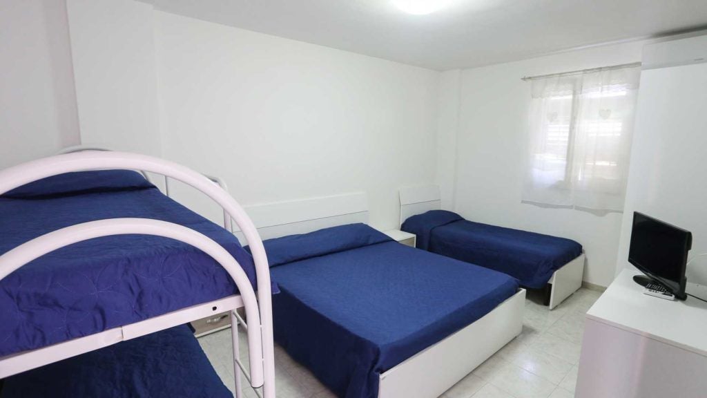 Une chambre avec trois lits superposés, un bureau avec un ordinateur et une fenêtre avec des rideaux.