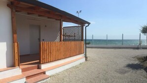 Un edificio frente a la playa con una terraza de madera y escalones que conducen a una entrada cubierta.