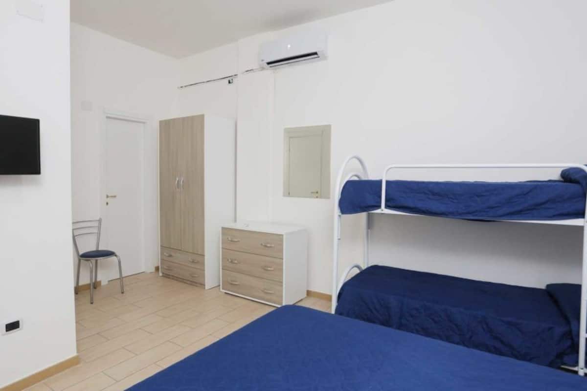 A bedroom with bunk beds, a desk, a chair, a wardrobe, and a TV.