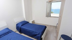 Una habitación con dos camas, una ventana con vista a la playa y un armario pequeño.