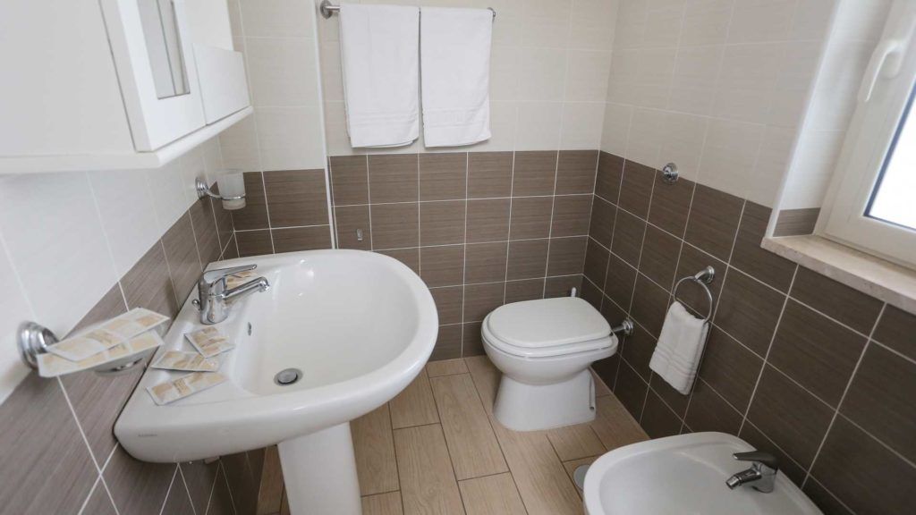 A bathroom with a sink, toilet, and bidet. There are two white towels hanging on the wall.