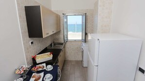 Cocina compacta con vista al mar, un refrigerador pequeño y una zona de comedor con pasteles.