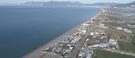 Vista aérea de una zona costera con una extensa playa, una carretera paralela a la orilla y una combinación de edificios residenciales y comerciales.