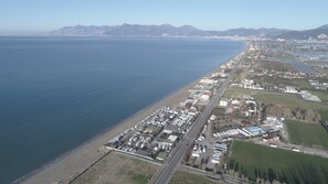 Vue aérienne d’une zone côtière avec une longue plage, une route parallèle à la plage et un mélange de bâtiments résidentiels et commerciaux.