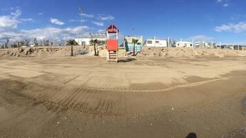 A sandy beach with a lifeguard tower and a row of buildings in the background.