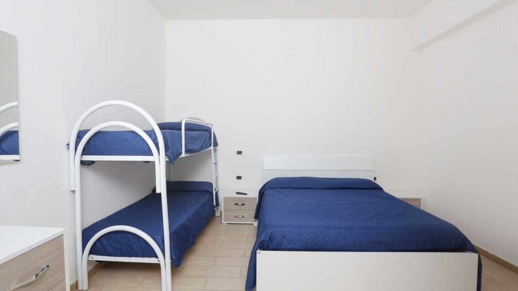 Une chambre avec des lits superposés, un bureau blanc et un miroir.