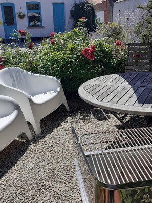 A patio area with a round wooden table, two white plastic chairs, and a metal grill. - Wetterdelle (Heers)
