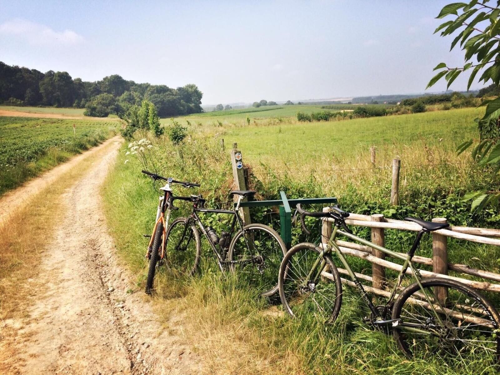 A dirt path leading through a rural landscape with bicycles parked by a wooden fence.