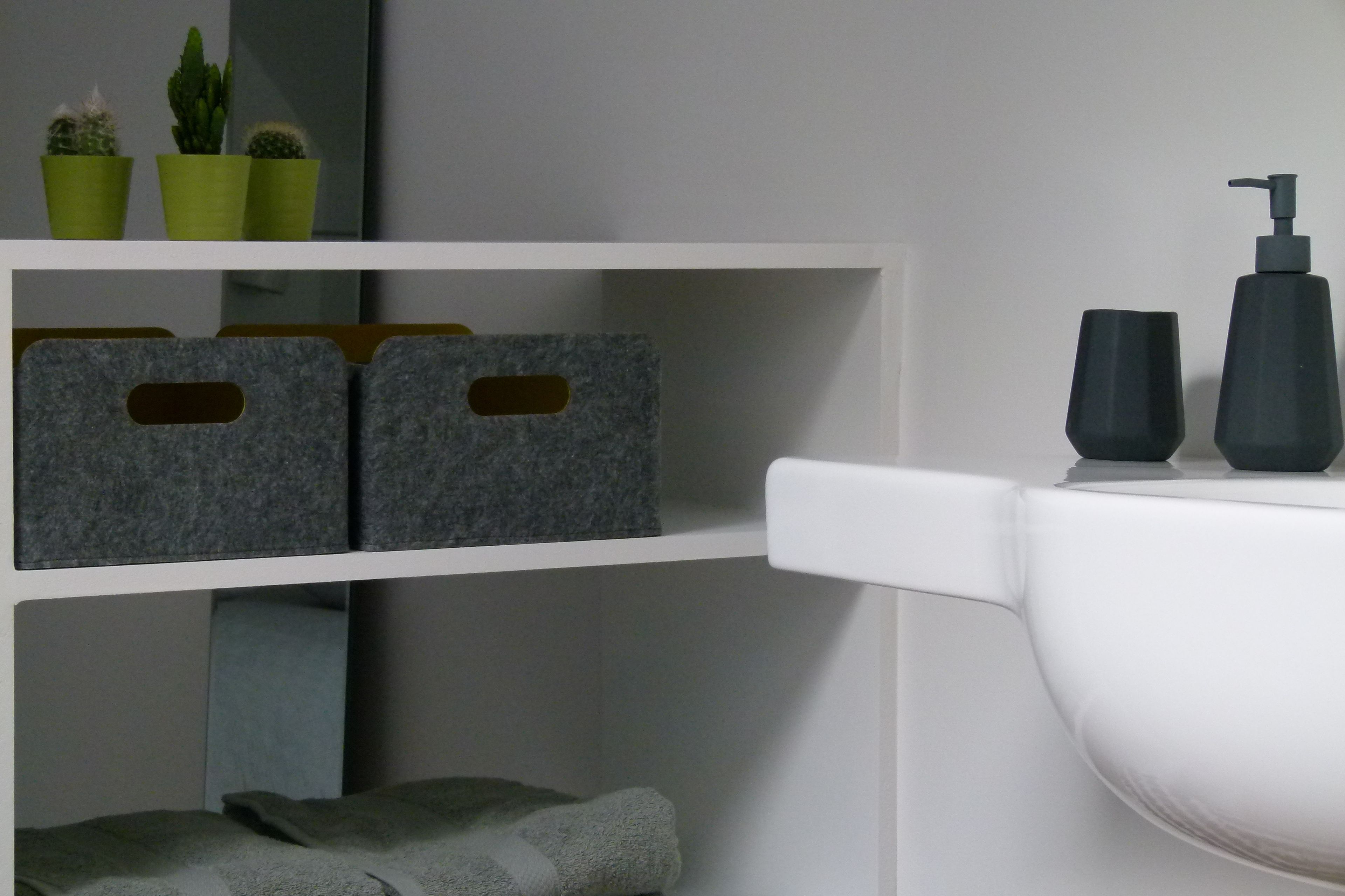 A bathroom with a white sink, black soap dispenser, and two black cups. There are three green potted plants on a shelf above the sink.