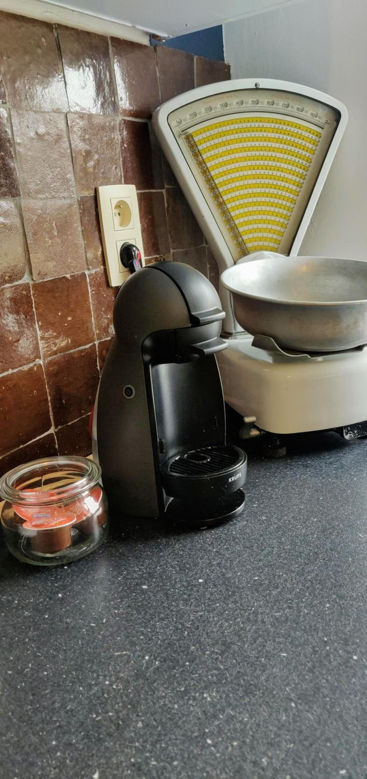 A kitchen with a coffee maker, a scale, and a jar of spices.