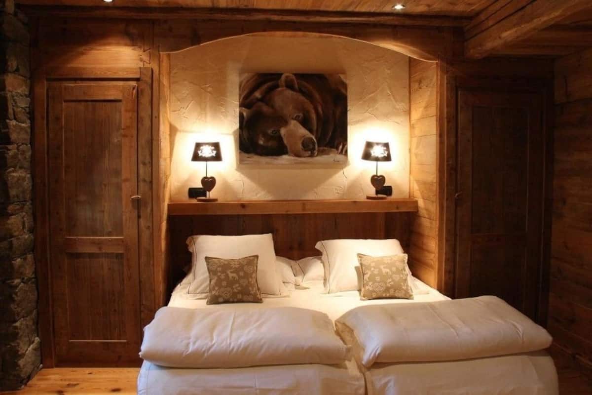 Ein gemütliches Zimmer mit Holzbalkendecke, einem großen Bett mit weißer Bettwäsche und gemusterten Kissen sowie einem Bärenbild über dem Bett.