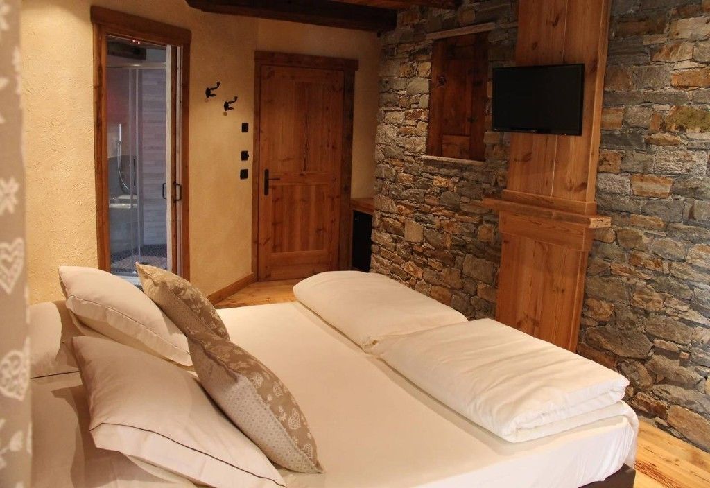 A room with a bed, a stone wall, wooden doors, and a television.