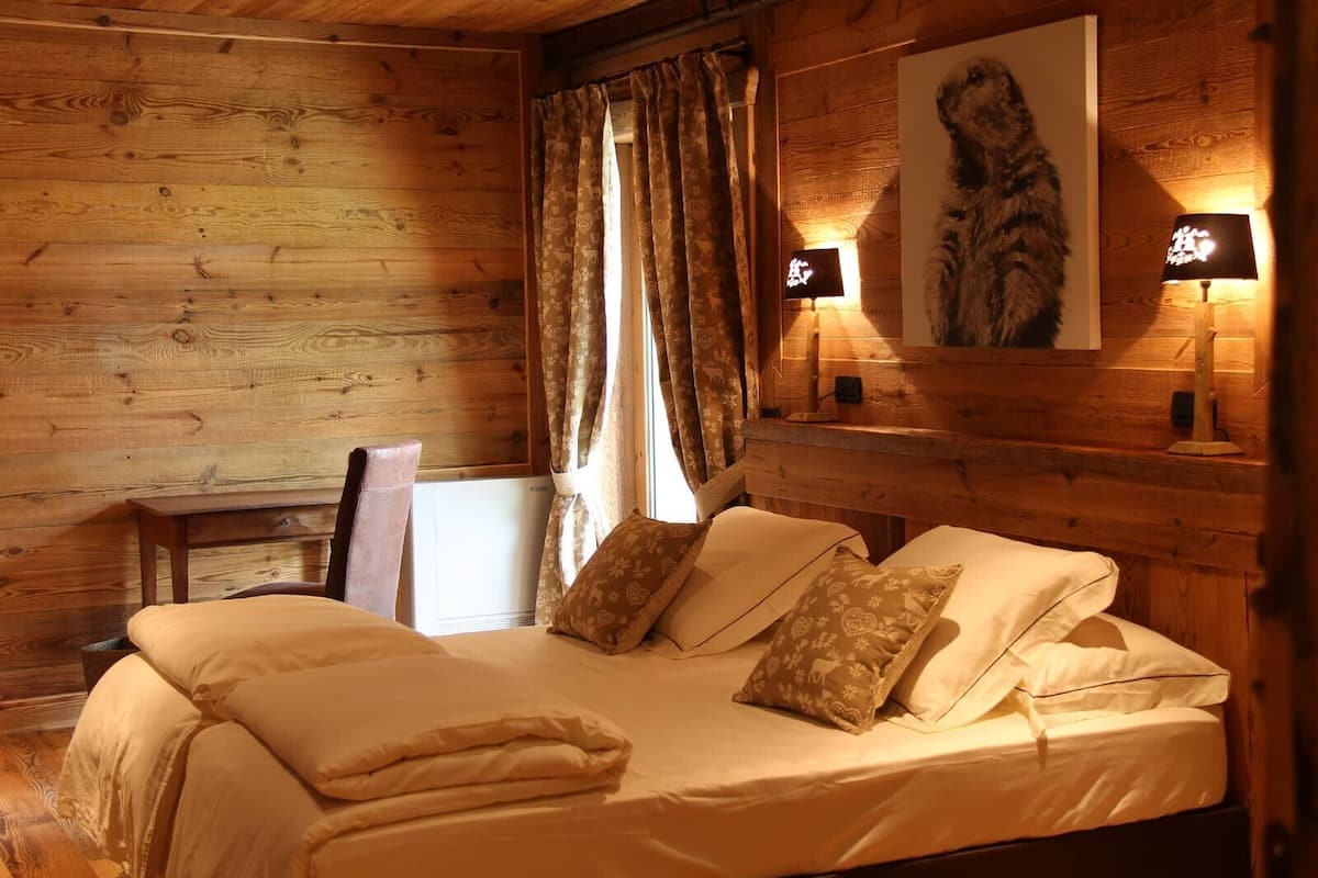 Ein gemütlicher Holzraum mit einem Bett, zwei Lampen, einem Sessel und einem gerahmten Bild an der Wand.