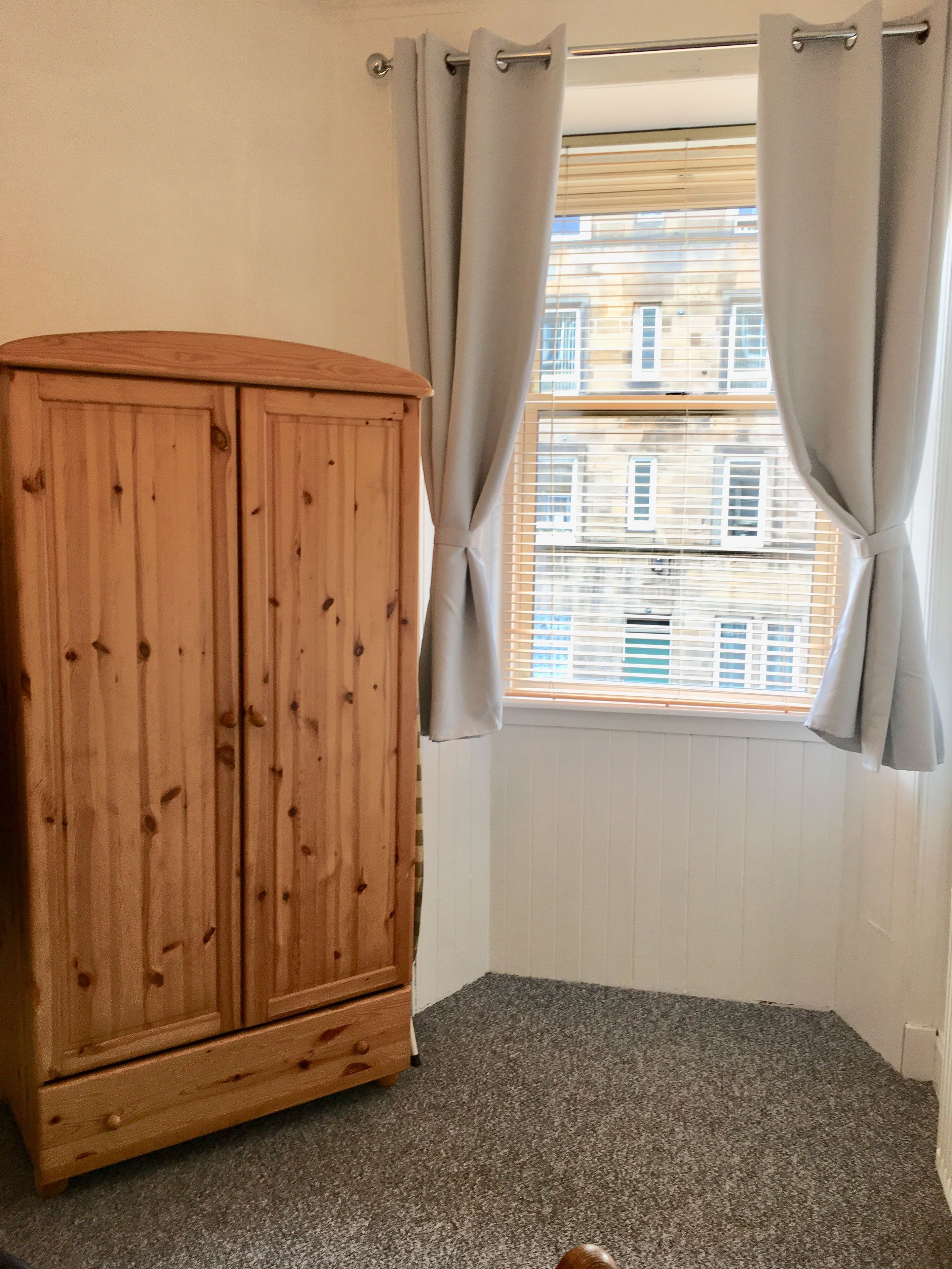 Une pièce avec une armoire en bois, une fenêtre avec des rideaux et une vue sur les bâtiments environnants.