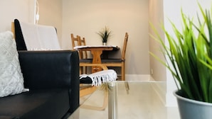 A modern living room with a black sofa, a wooden dining table, and a potted plant. - Easter Road Edinburgh Apartment (Edinburgh)