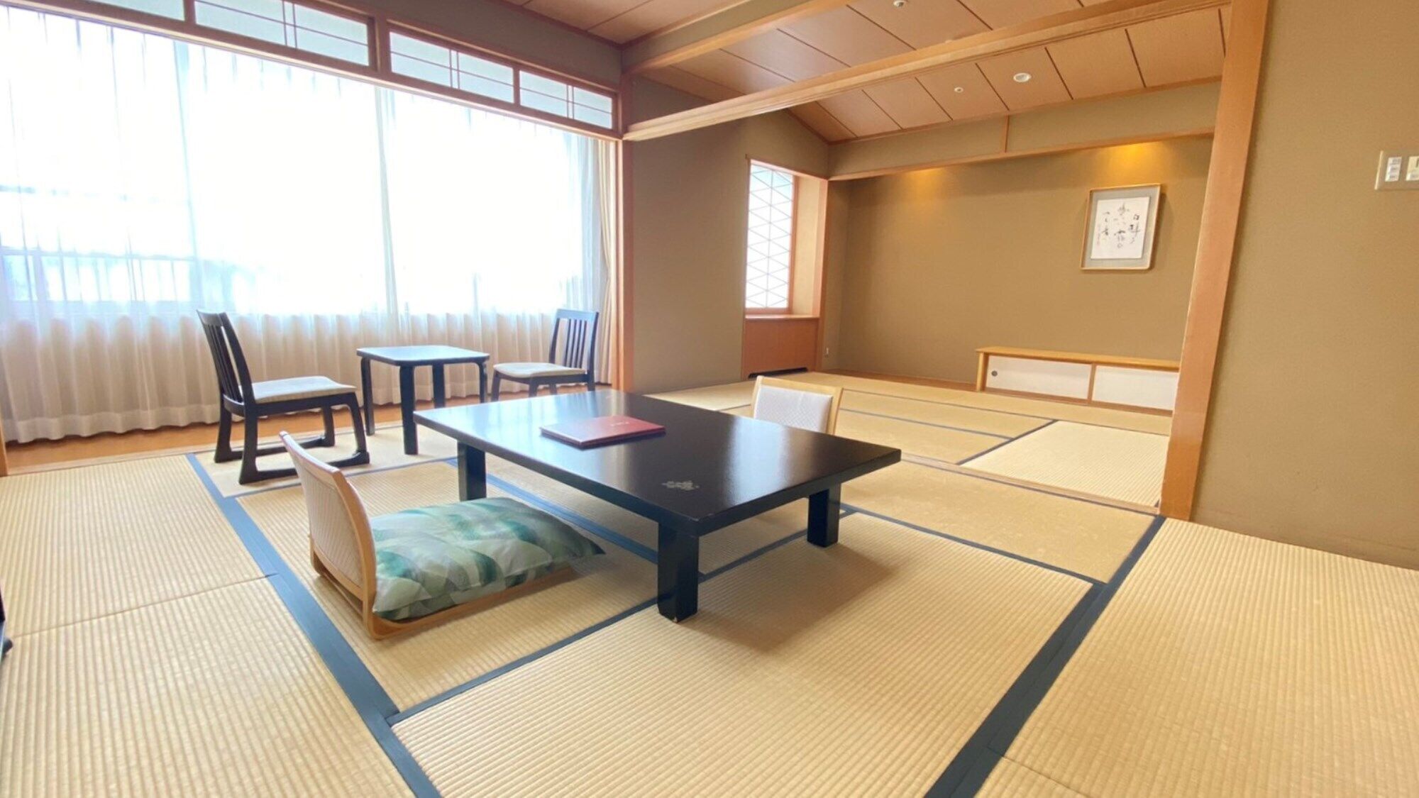 A tatami mat room with a low table, chairs, and a futon bed.