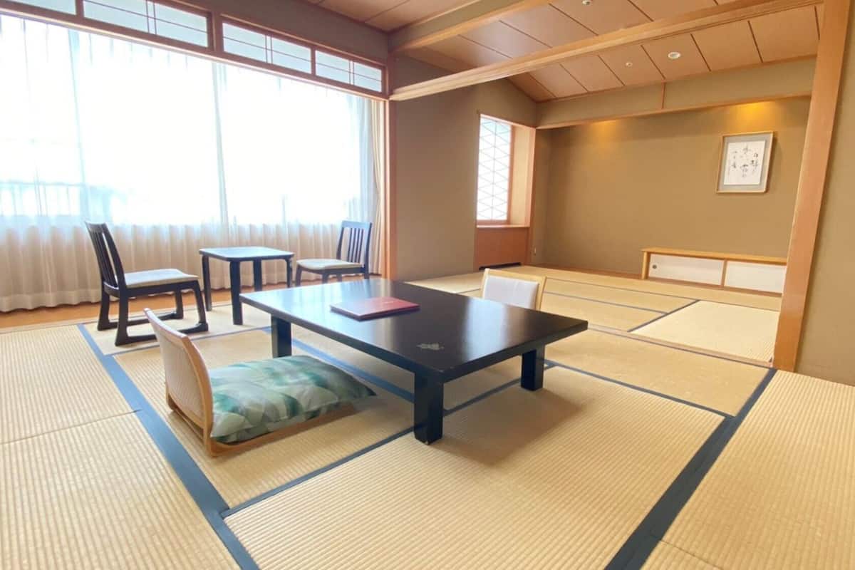 A tatami mat room with a low table, chairs, and a futon bed.