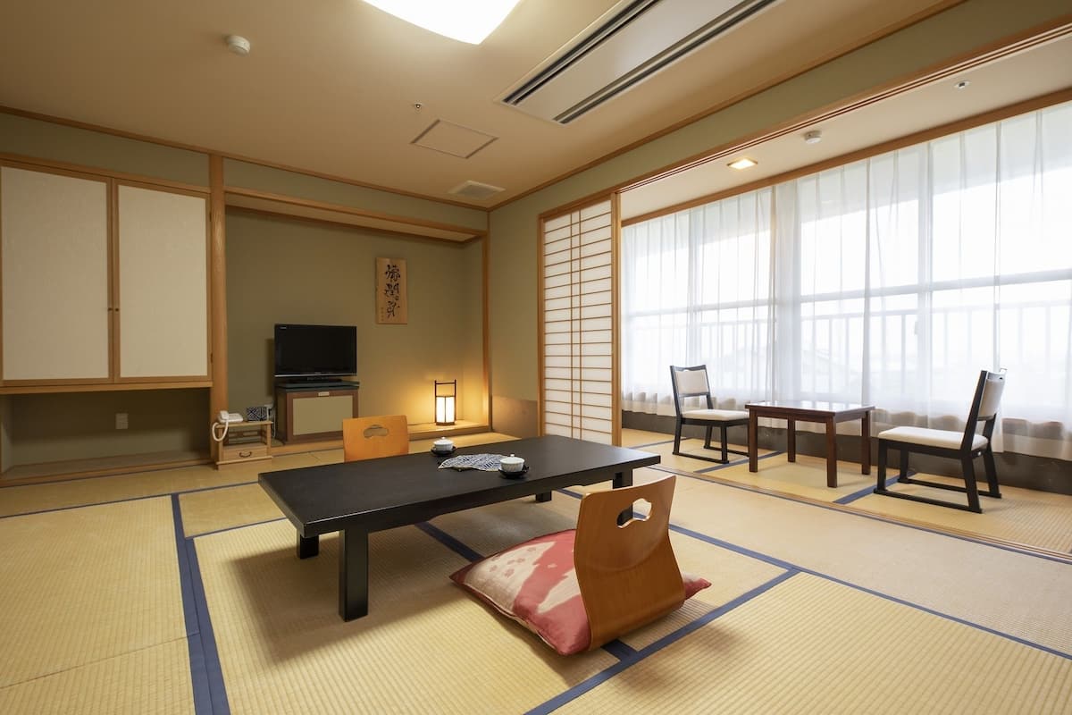 A traditional Japanese room with tatami flooring, a low table, chairs, a television, and sliding doors.