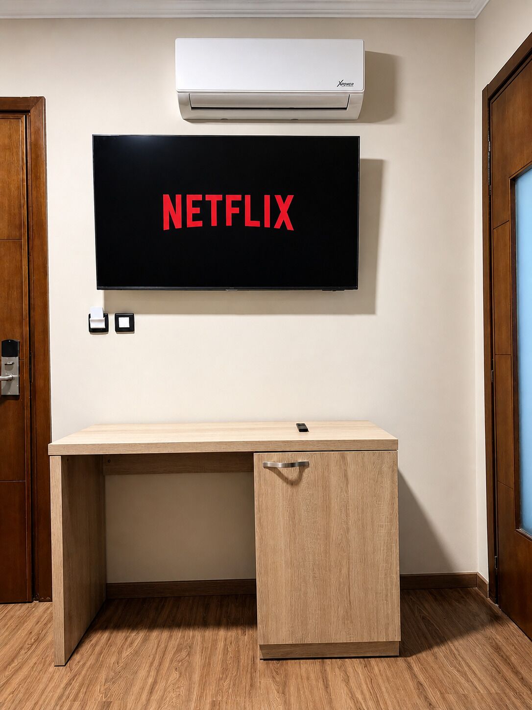 Une pièce avec un bureau en bois, un climatiseur fixé au mur et un téléviseur mural affichant le logo « NETFLIX ».