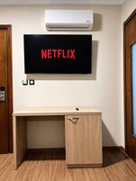 Una habitación con un escritorio de madera, aire acondicionado instalado y un televisor de pared mostrando 'NETFLIX'.