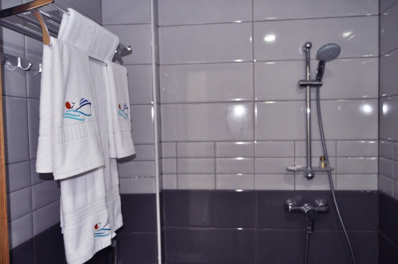 Un baño con paredes de azulejos blancos, suelo negro y una zona de ducha con ducha de mano.