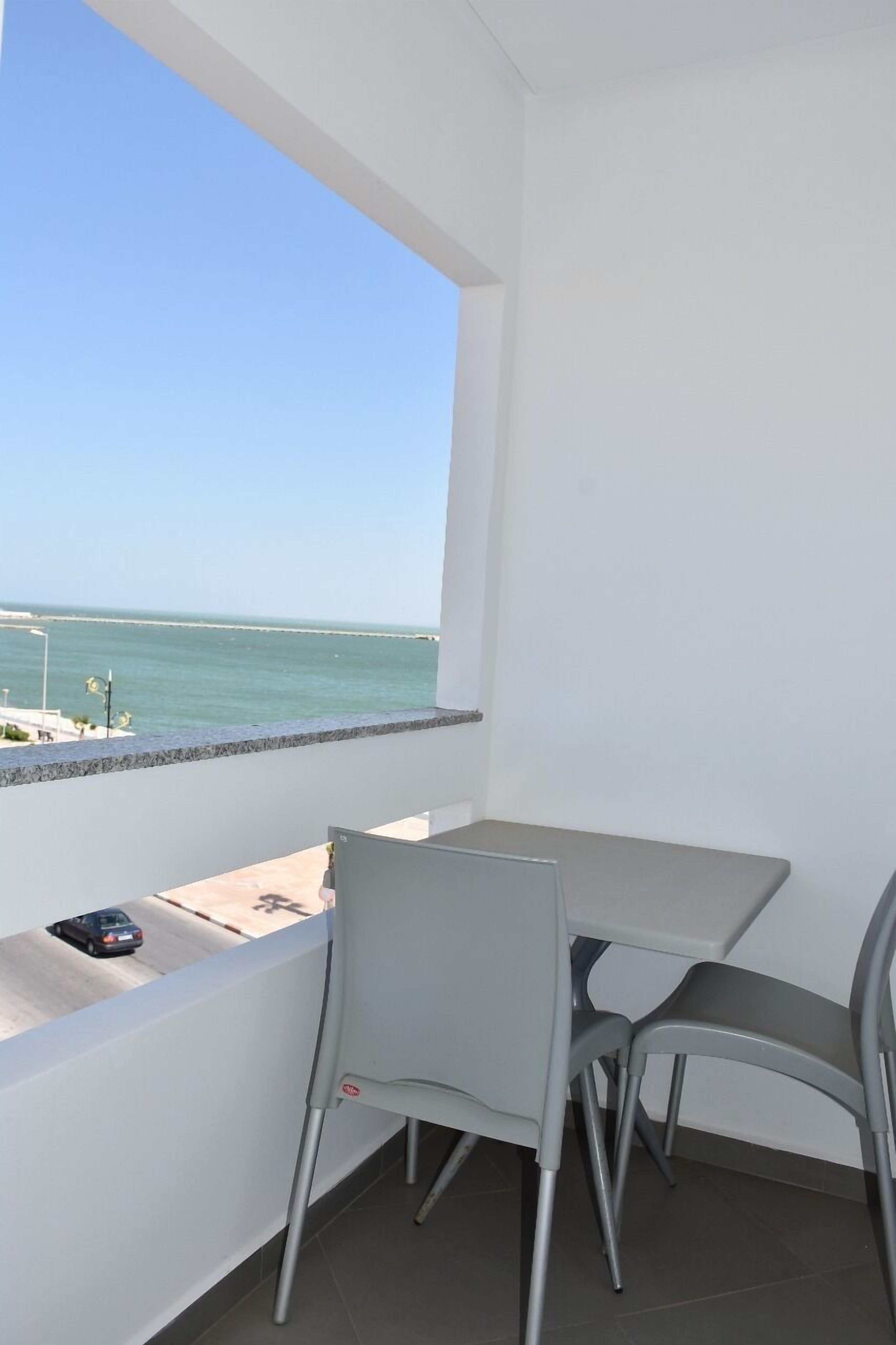 A balcony with a view of the sea, a table, and two chairs.