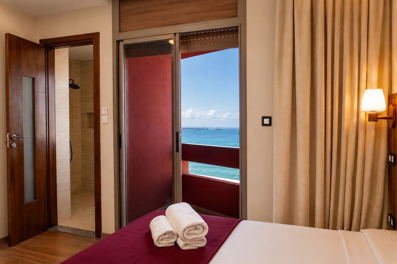 Habitación de hotel con cama, baño con ducha y balcón con vistas al mar.