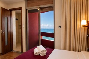 Habitación de hotel con cama, baño con ducha y balcón con vistas al mar.