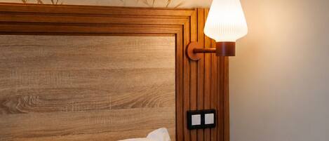 Habitación de hotel con cabecera de madera, cama con ropa blanca, lámpara de noche y pared con estampado de hojas de bambú.